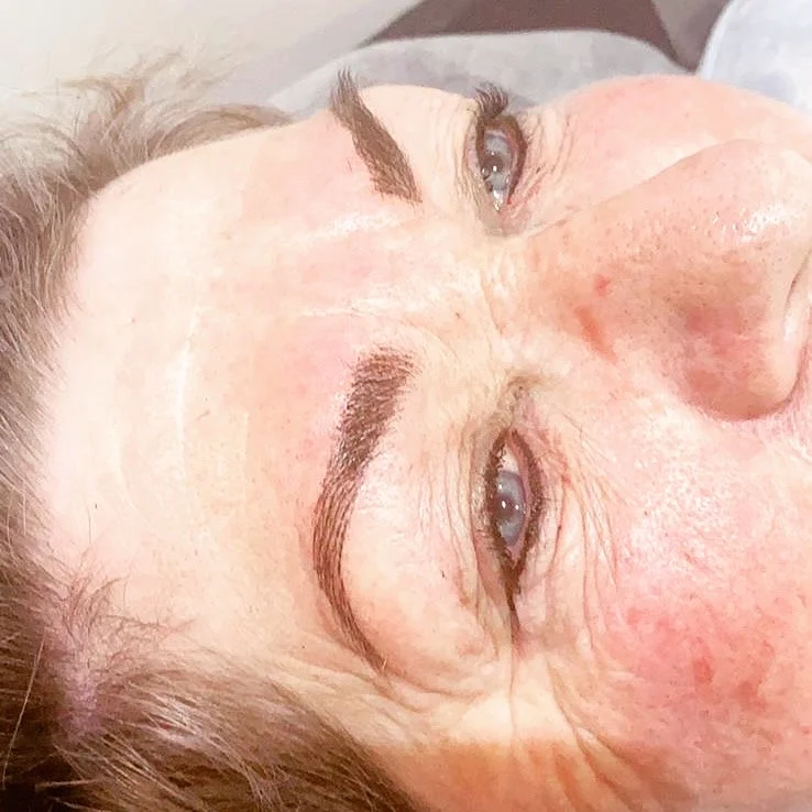 Reclining client's freshly tattooed brows in close-up, soft feathered strokes