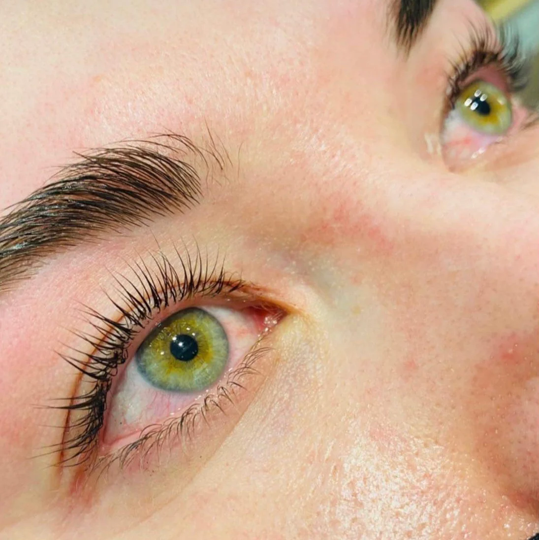Green-hazel eyes after a lash lift, natural lashes curled upward, brows brushed up