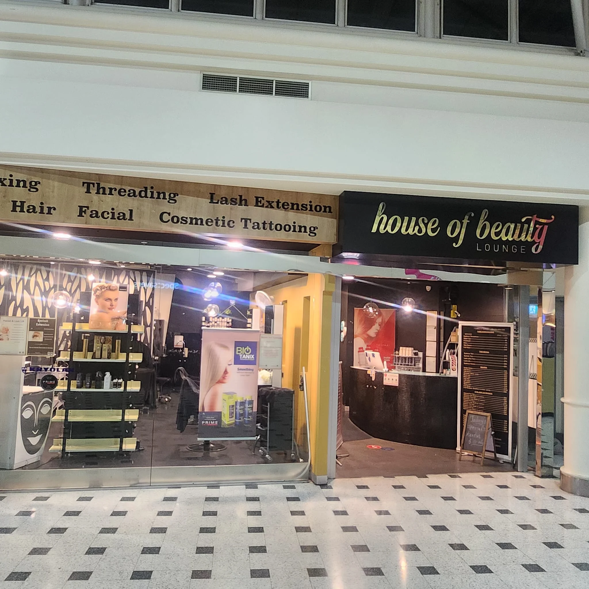 Dandenong Plaza shopfront — illuminated house of beauty LOUNGE fascia, timber service board, reception counter and chequerboard mall floor